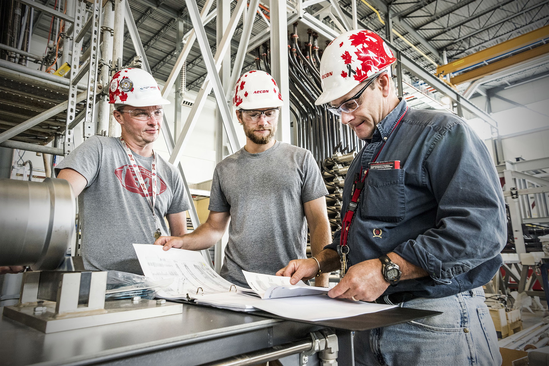 Aecon Workers In Hardhats and Blueprints 